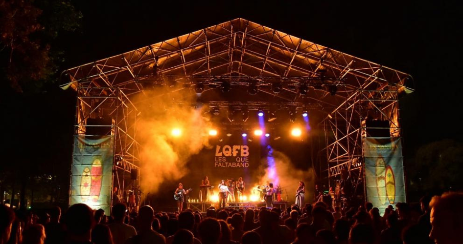 Outdoor night concert with a band performing on a lit stage and a crowd watching.
