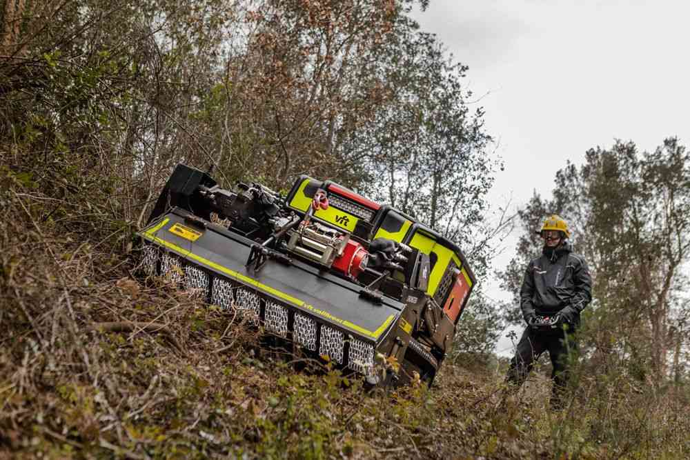 All-terrain rescue vehicle on a dirt slope, with a firefighter in a yellow helmet standing nearby in protective gear.